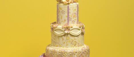 Un pastel de varios niveles con decoraciones florales y un lazo, sobre un fondo amarillo.