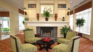 A lobby with a fireplace, four armchairs, a coffee table, and decorative plants. - Hilton Garden Inn Tulsa Airport (Tulsa)