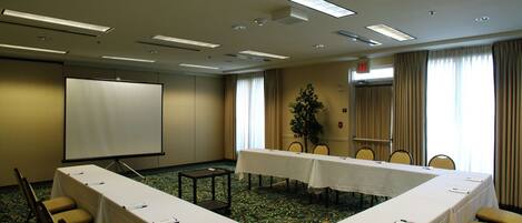 A conference room with a long table, chairs, a projector screen, and a plant.