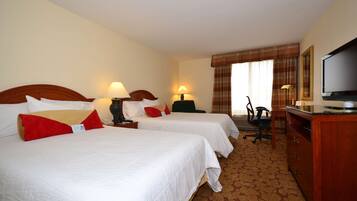 A hotel room with two beds, a desk, a television, and a chair.