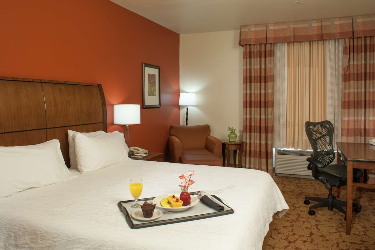 A hotel room with a bed, a dining table, a chair, a lamp, and a tray with breakfast items.