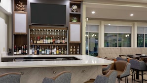 Un espace bar doté d’un long comptoir, de plusieurs options de sièges, notamment des tabourets de bar et des fauteuils rembourrés, et d’un téléviseur fixé au-dessus du bar.