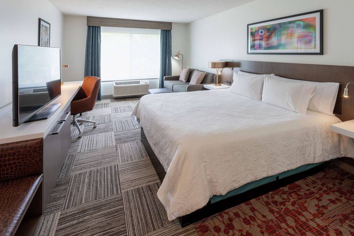 Een hotelkamer met een groot bed, een bureau met een flatscreen televisie, een stoel, een bank, een lamp en een schilderij aan de muur.