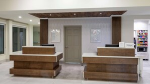 Un espace d’accueil d’hôtel comprenant deux comptoirs de réception en bois, une porte et un distributeur automatique.
