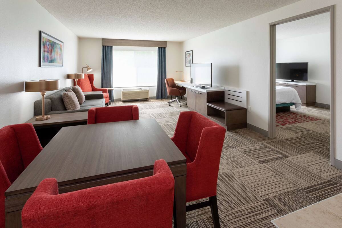 Een hotelkamer met een eethoek, een bureau met een computer, een televisie en een bed.