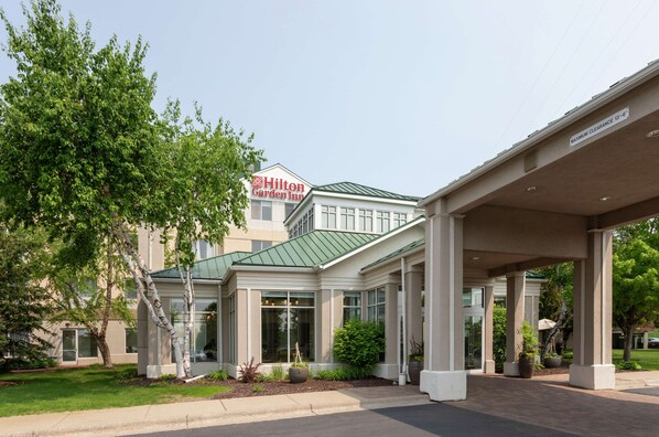 Un Hilton Garden Inn con entrada cubierta, ventanas amplias y techo verde.