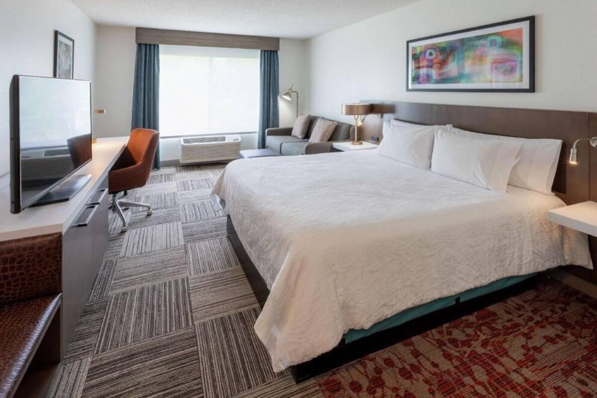 Een hotelkamer met een bed, een bureau met een televisie, een stoel, een bank en een schilderij aan de muur.