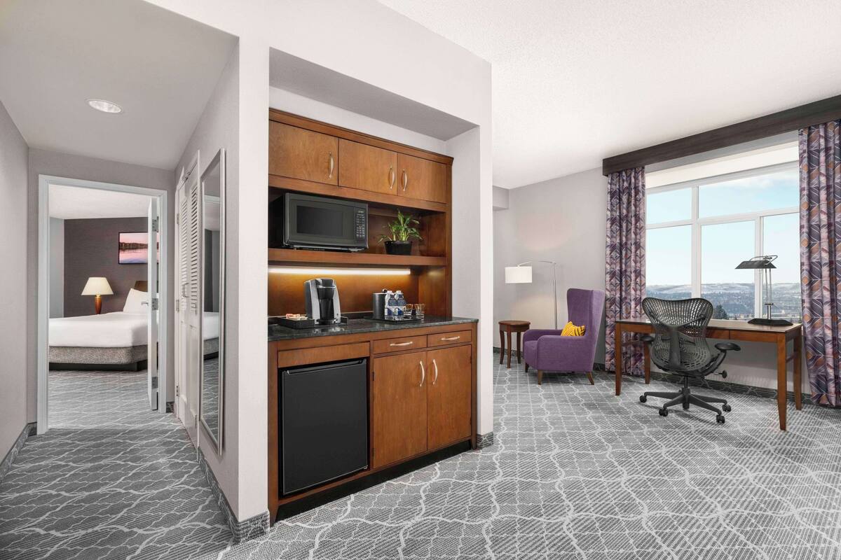 Habitación de hotel compacta con kitchenette, cama, escritorio y vistas a la ciudad.
