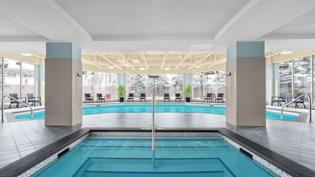 An indoor swimming pool with clear water, surrounded by lounge chairs and potted plants. - Hilton Garden Inn Calgary Airport (Calgary)