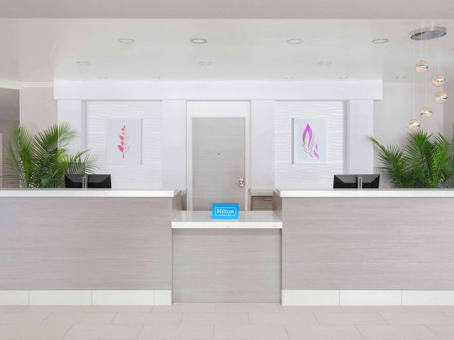 A modern hotel reception desk with a minimalist design, featuring two reception counters, a digital sign, and framed artwork on the walls.