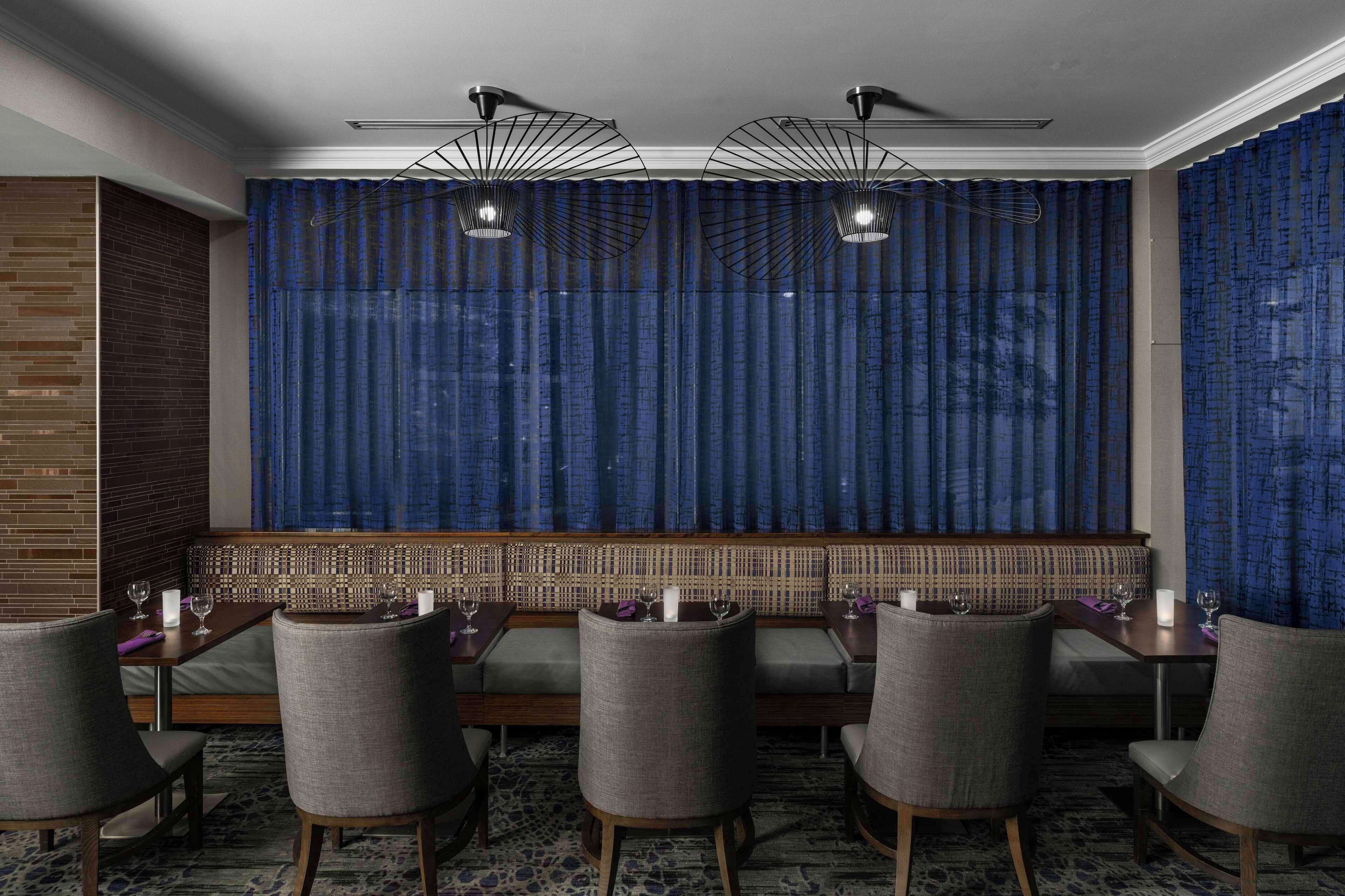 A restaurant with a high ceiling, patterned curtains, and a seating area with tables and chairs.