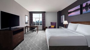 A hotel room with a large bed, a desk, a chair, a TV, and a window with a city view. - Hilton Garden Inn Calgary Airport (Calgary)