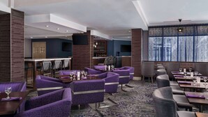 A modern hotel lobby with purple upholstered seating, a bar area, and a large window with curtains. - Hilton Garden Inn Calgary Airport (Calgary)