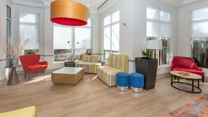 A spacious living area with a large window, a red sofa, a yellow and white striped sofa, a wooden coffee table, and a blue ottoman. - Hilton Garden Inn St. Augustine Beach (St. Augustine)