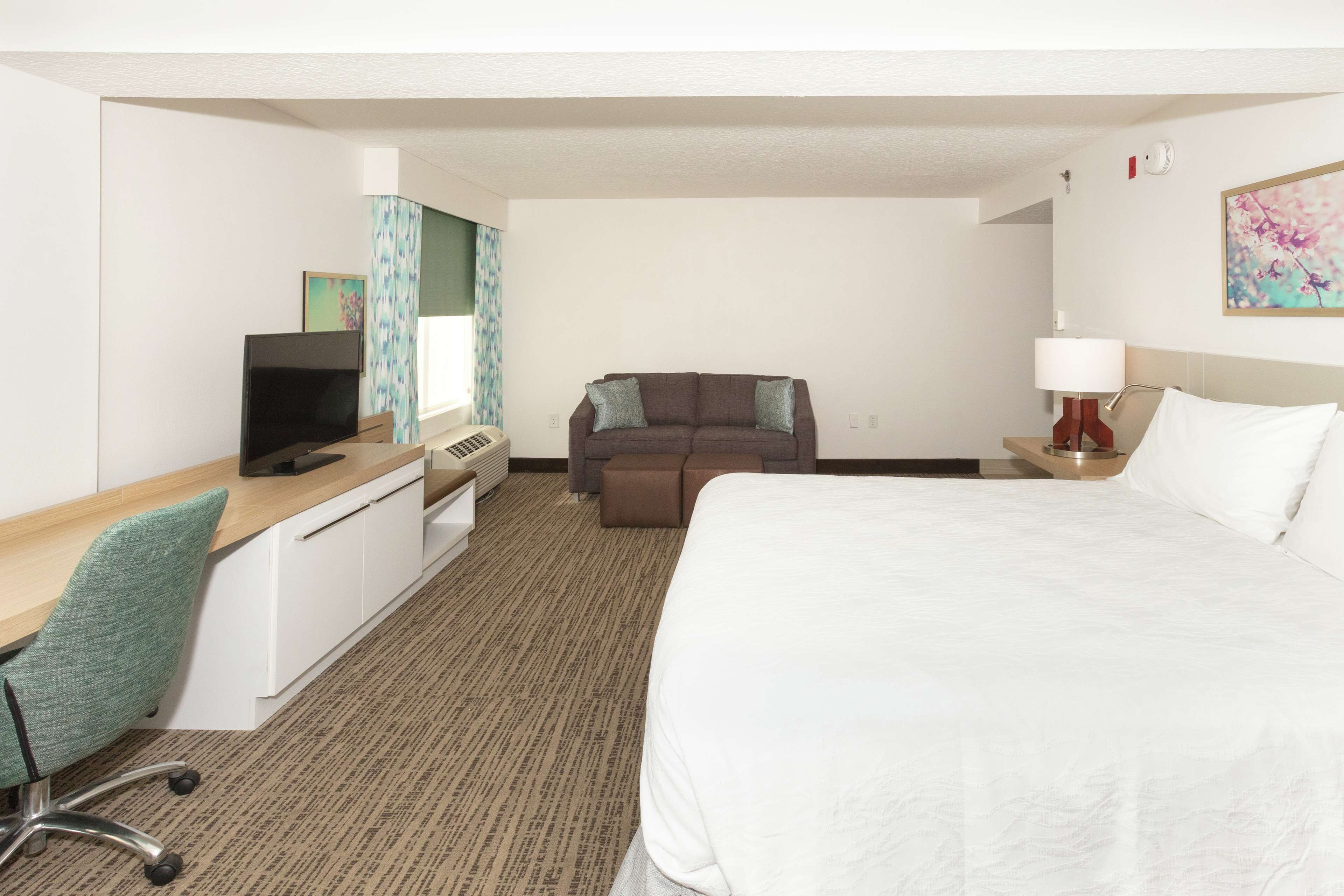 Quarto de hotel com uma cama grande, uma escrivaninha com um computador, um sofá e uma televisão.