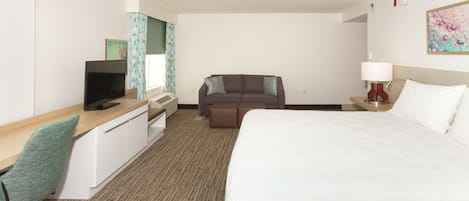 Quarto de hotel com uma cama grande, uma escrivaninha com um computador, um sofá e uma televisão.
