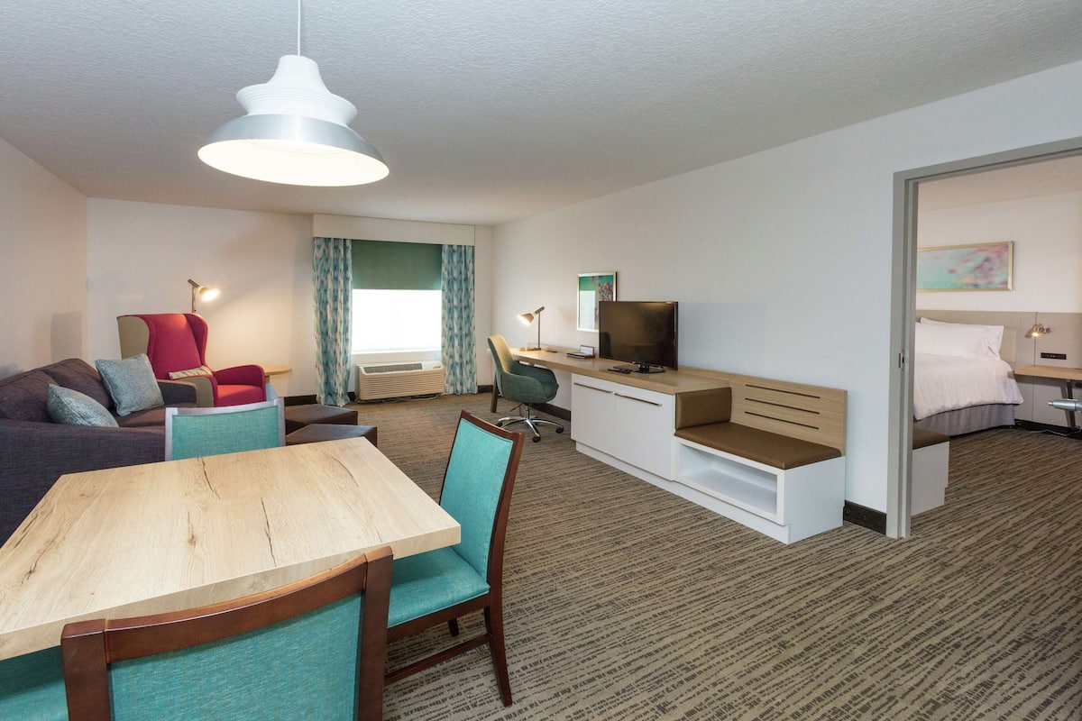 A modern hotel room with a dining area, a TV, a desk, and a bed.