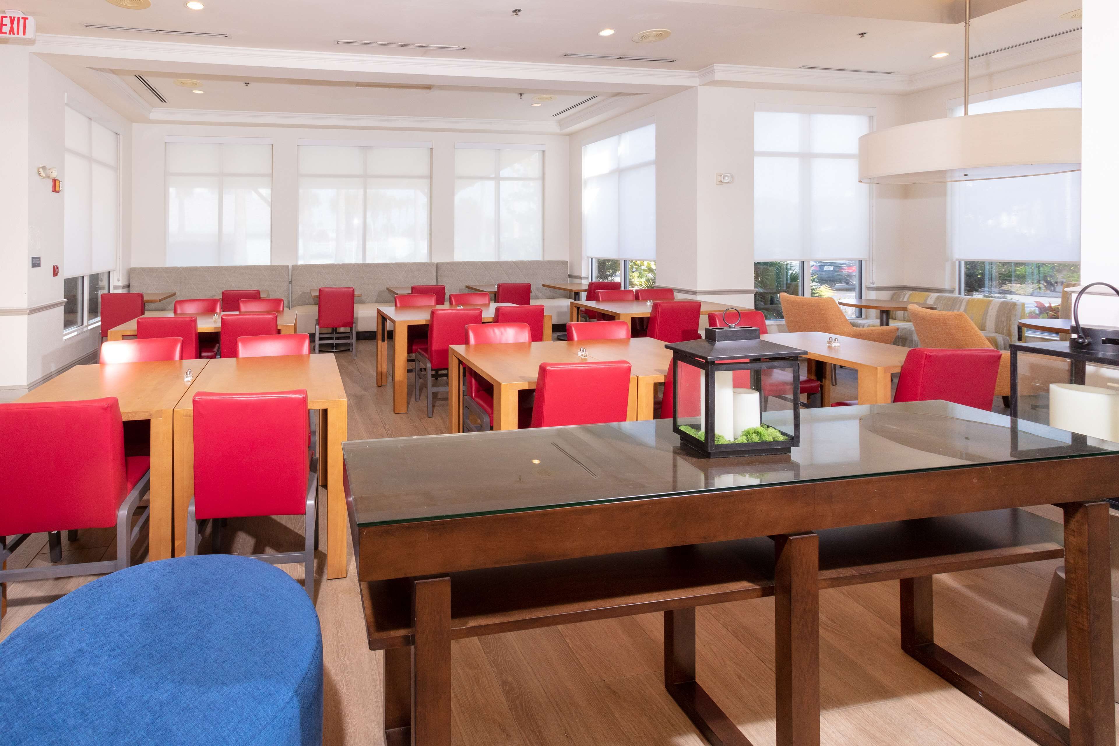 A modern dining area with red chairs, wooden tables, and large windows.