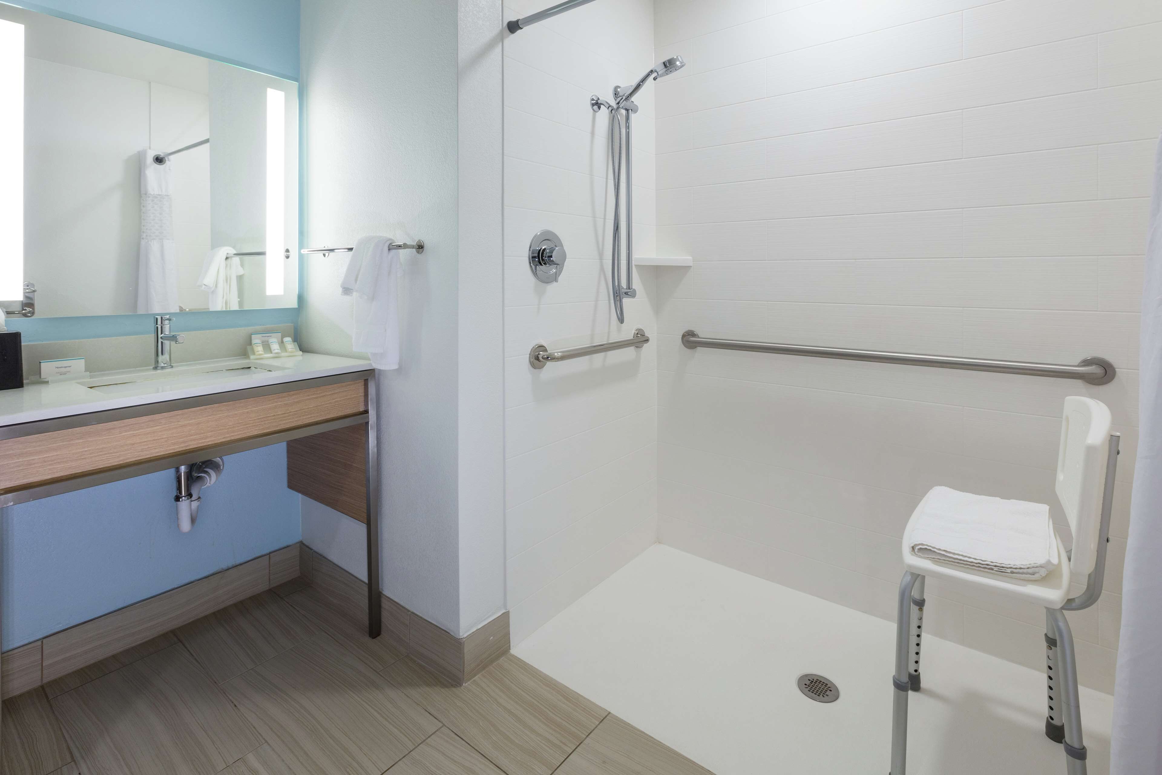 A modern bathroom with a shower, grab bars, a sink, and a toilet.