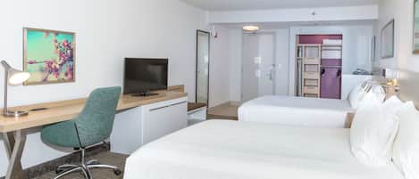 Ein Hotelzimmer mit Schreibtisch, zwei Betten, Fernseher, Stuhl und Badezimmertür.
