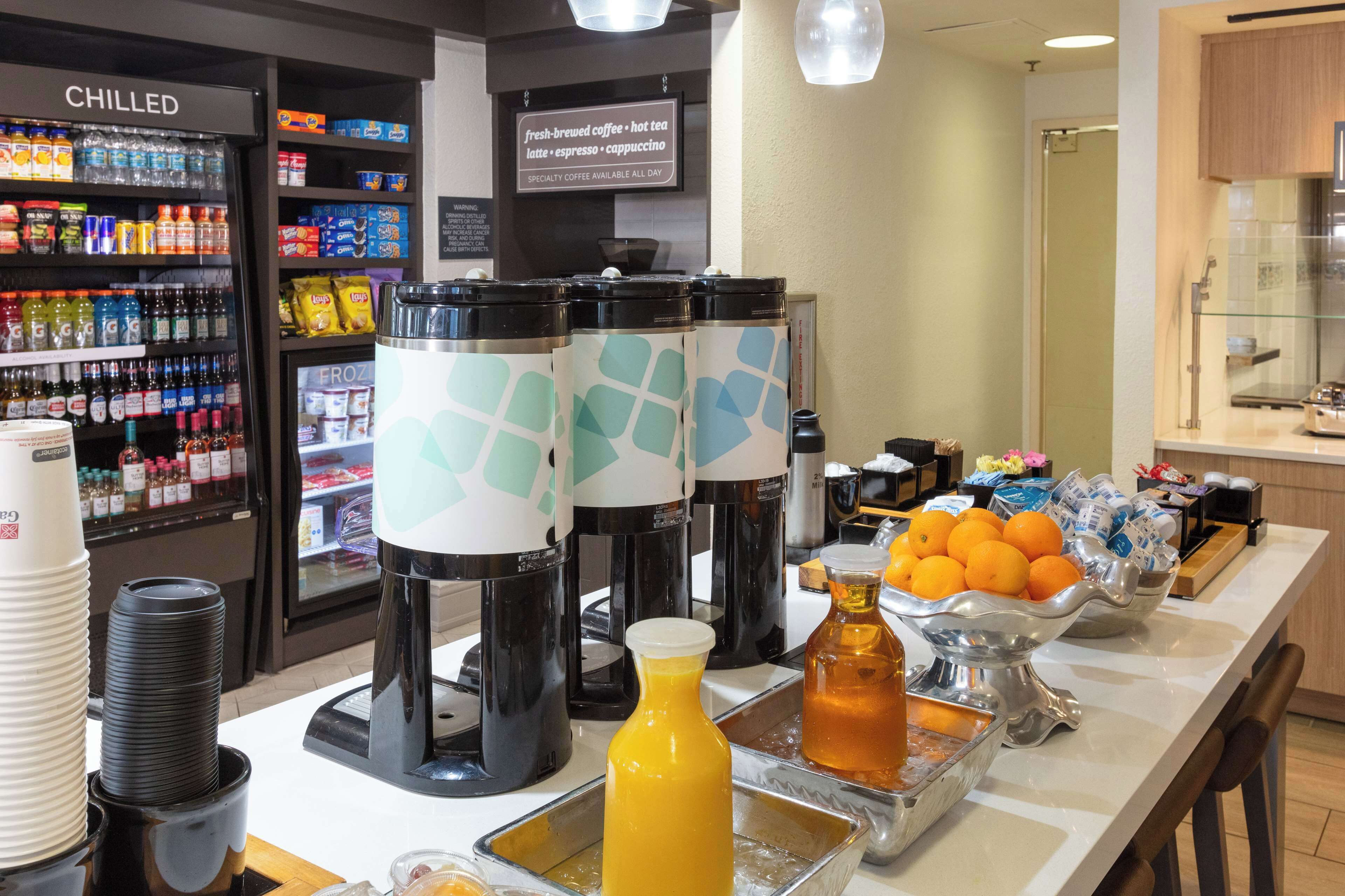 A breakfast bar with coffee machines, a chilled beverage fridge, and a fruit bowl.