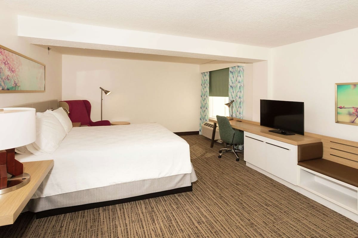 A hotel room with a bed, desk, TV, and a chair.