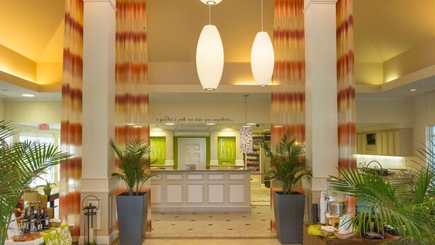 A hotel lobby with a reception desk, large potted plants, and hanging pendant lights. - Hilton Garden Inn St. Augustine Beach (St. Augustine)