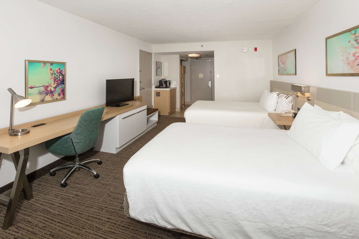 A hotel room with two beds, a desk with a chair, a television, and artwork on the walls.