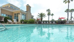 A clear swimming pool with lounge chairs and umbrellas, surrounded by palm trees and a building with large windows. - Hilton Garden Inn St. Augustine Beach (St. Augustine)
