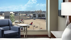 A hotel room with a large window offering a view of an airport, including parked airplanes and airport buildings.