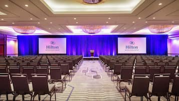 Un salón de conferencias amplio con filas de sillas apuntando a un escenario con una gran pantalla que muestra el logotipo de Hilton.