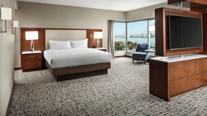 A hotel room with a large bed, a TV, a desk, and a view of the city.
