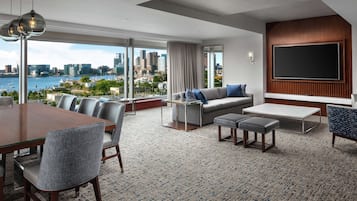 Una sala de estar moderna con un televisor grande, asientos cómodos, un comedor y vistas a un horizonte urbano y al agua.