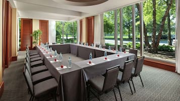 Une salle de conférence dotée d’une longue table, de chaises et de grandes fenêtres donnant sur des arbres et un parking.