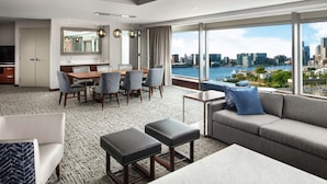 A modern hotel room with a dining area, a sofa, and a view of the city skyline.