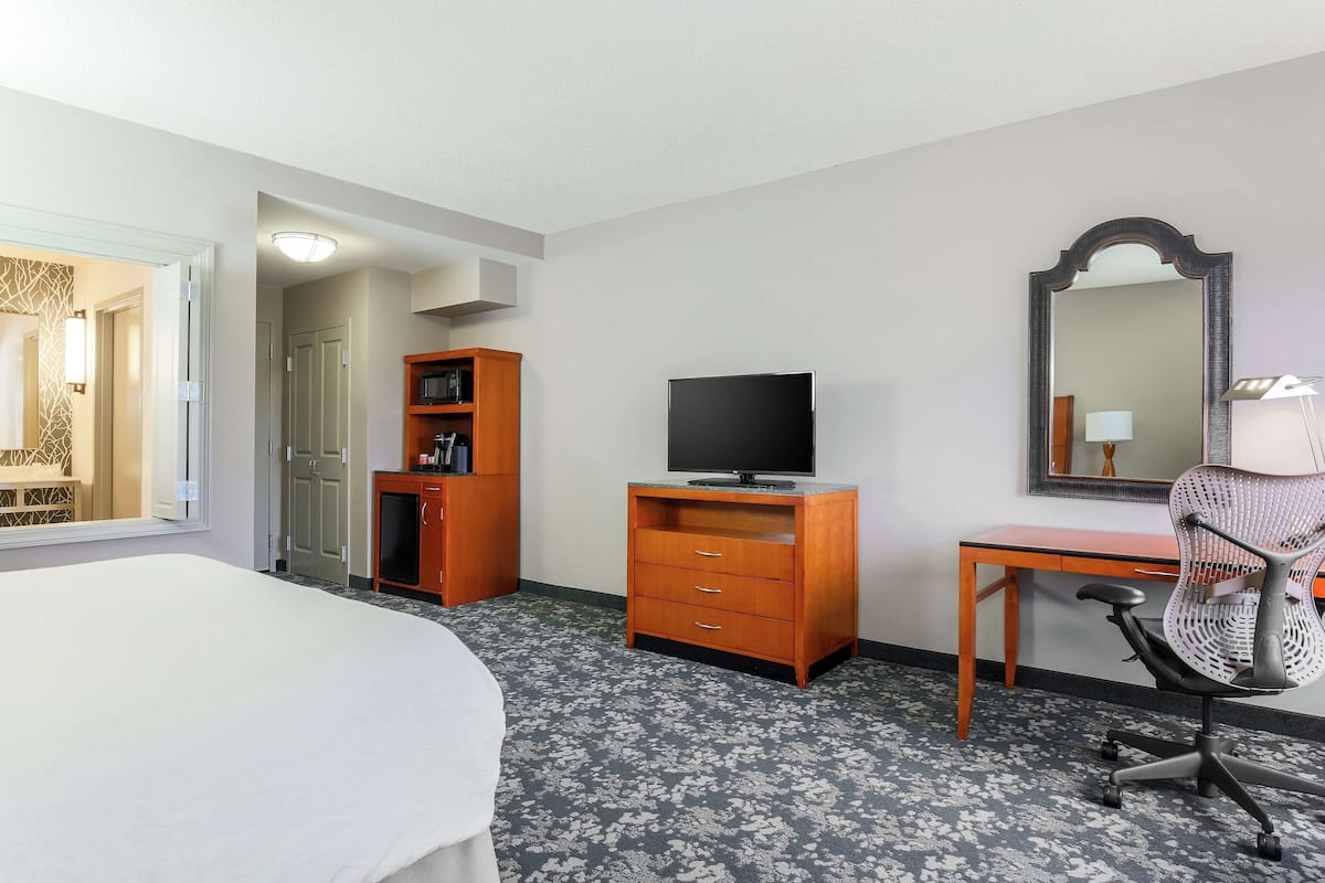 A hotel room with a bed, a desk with a computer, a TV, a wardrobe, and a mirror.