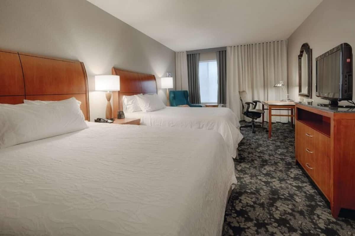 A hotel room with two beds, a desk, a chair, a television, and a dresser.