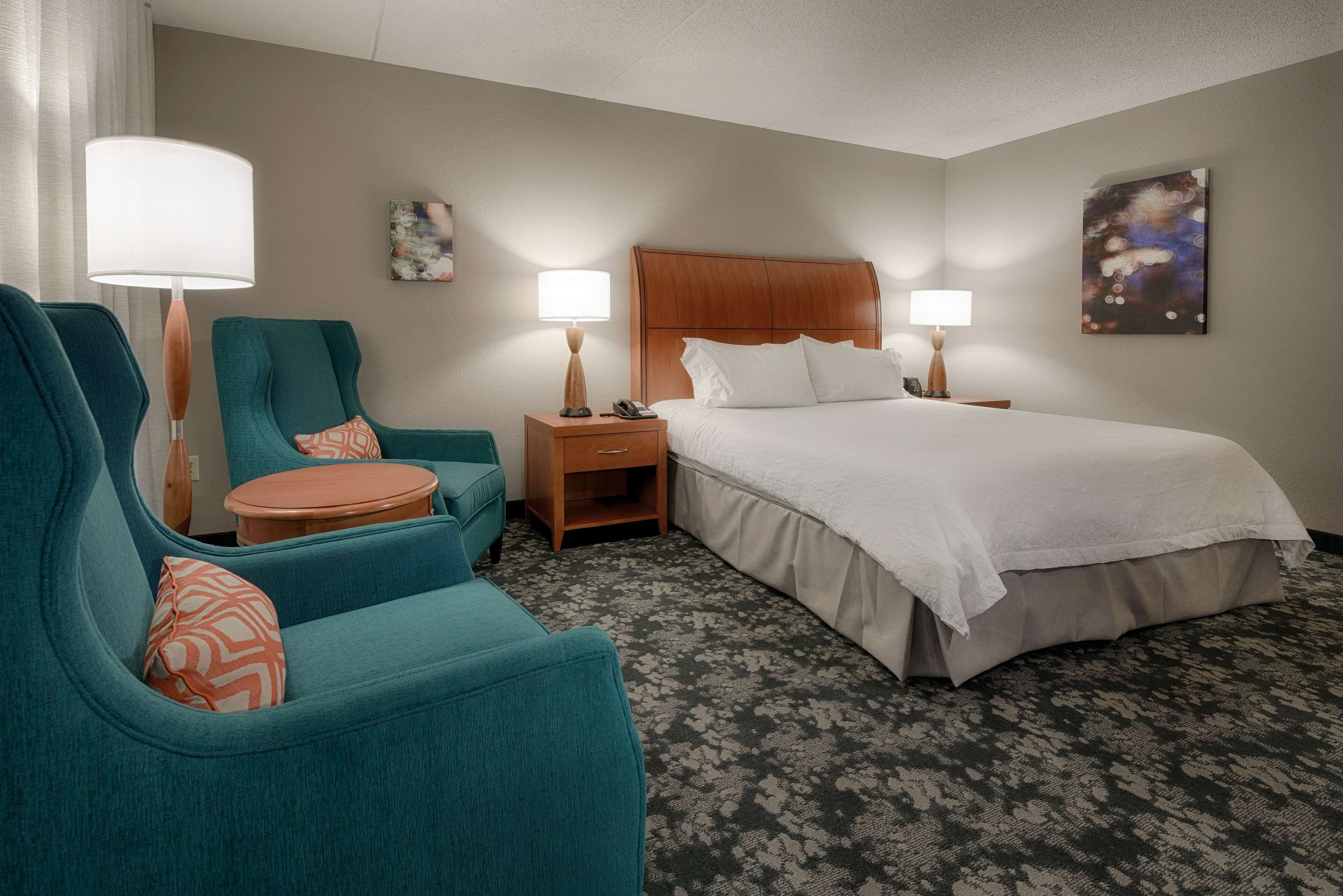 A hotel room with a large bed, two armchairs, a small table, and two bedside lamps.