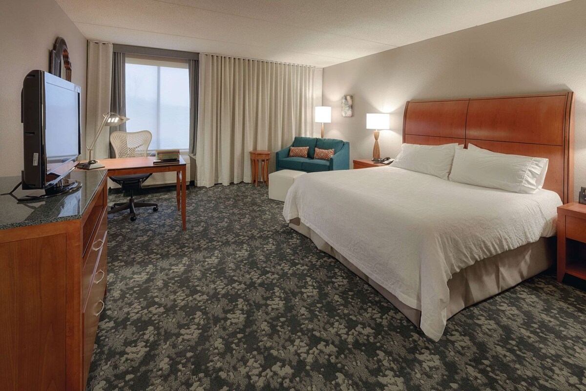 A hotel room with a bed, desk, chair, and a television.