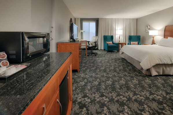 Habitación de hotel con cama, escritorio, microondas, televisor y dos sillas.