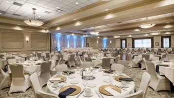 Une vaste salle de banquet avec des tables rondes dressées pour le repas, ornées de nappes blanches, de couverts dorés et blancs, et de chaises de couleur beige.