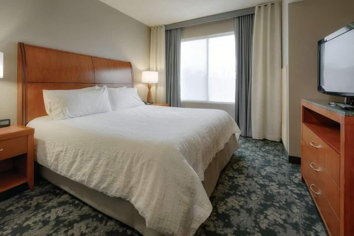 A hotel room with a large bed, a TV, a desk, and a window with curtains.