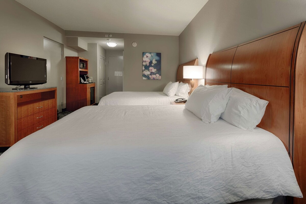A hotel room with two beds, a TV, a desk, and a painting on the wall.