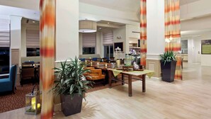 Um hall amplo com área de estar, balcão de recepção e uma grande planta.