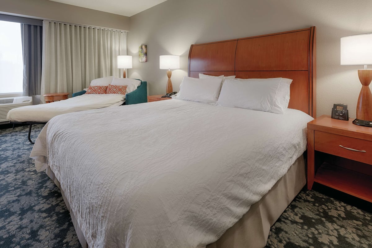 A hotel room with a large bed, two bedside tables, a chair, and a window with curtains.