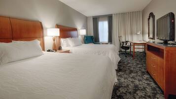 A hotel room with two beds, a desk, a chair, a TV, and a dresser.