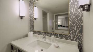 Un baño moderno con un lavabo blanco, un espejo grande y un revestimiento de pared estampado.