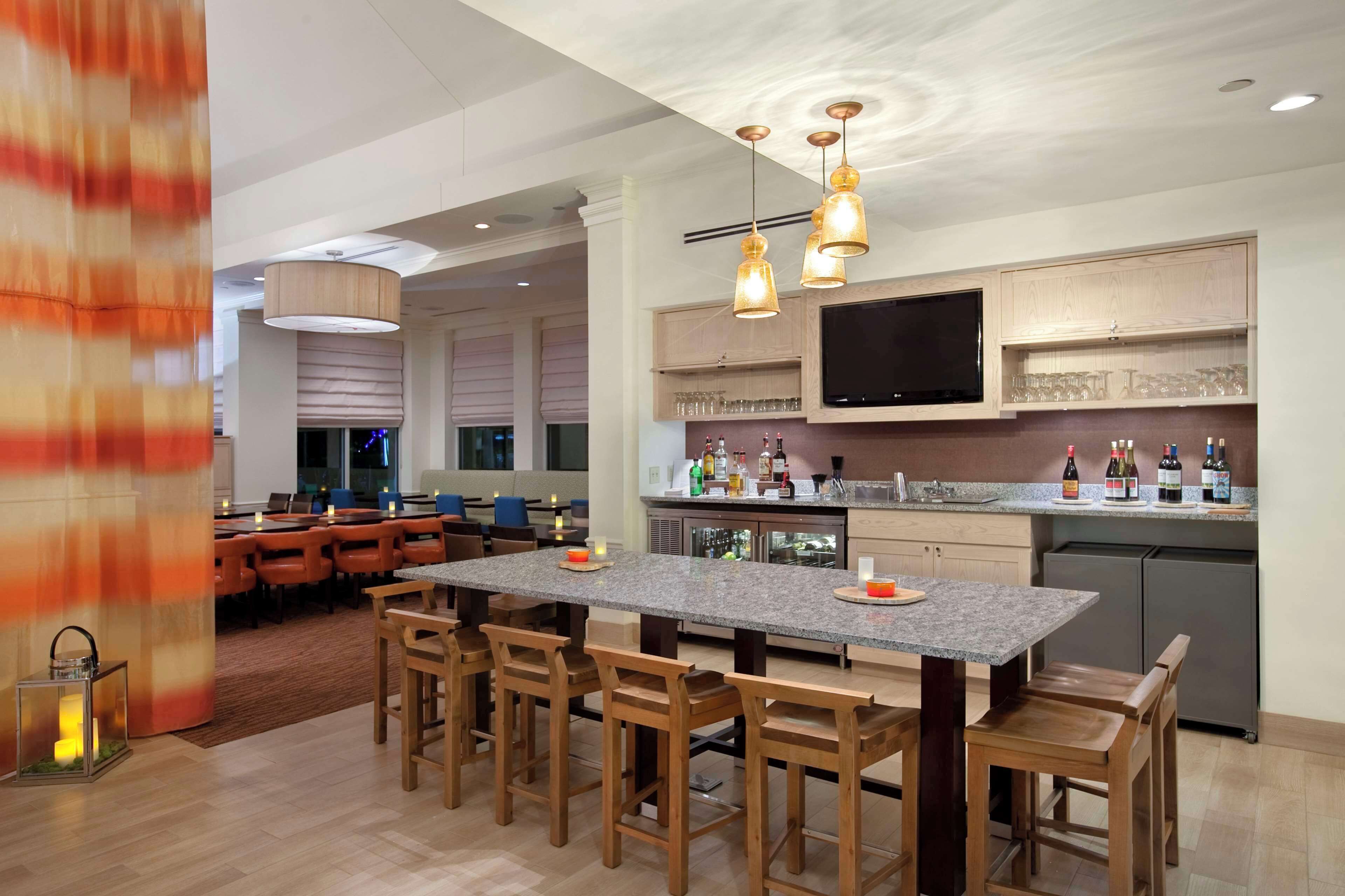 Uma cozinha moderna com uma ilha grande, banquetas de madeira e uma TV de tela plana fixada acima do balcão.