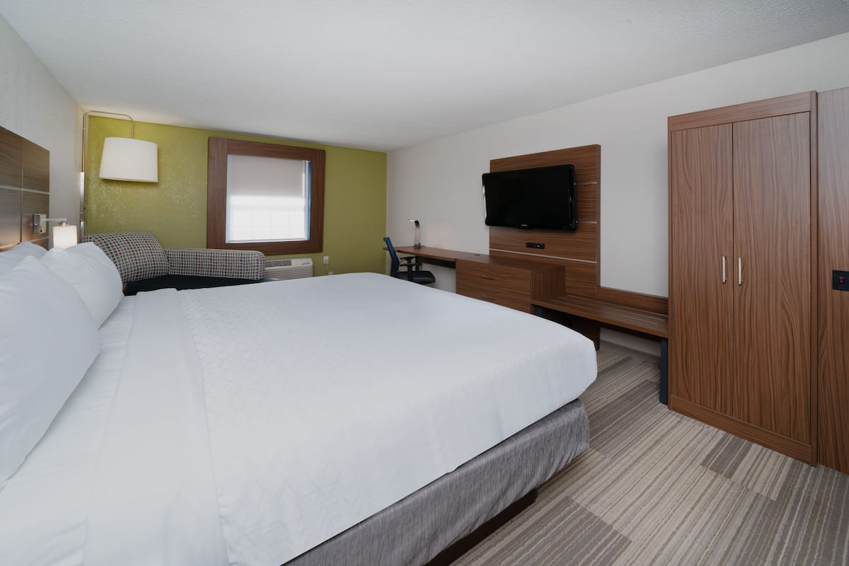 A hotel room with a large bed, a desk with a chair, a television, and a wardrobe.