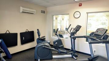 A fitness room with exercise equipment, a wall clock, and a window with a view of a building.